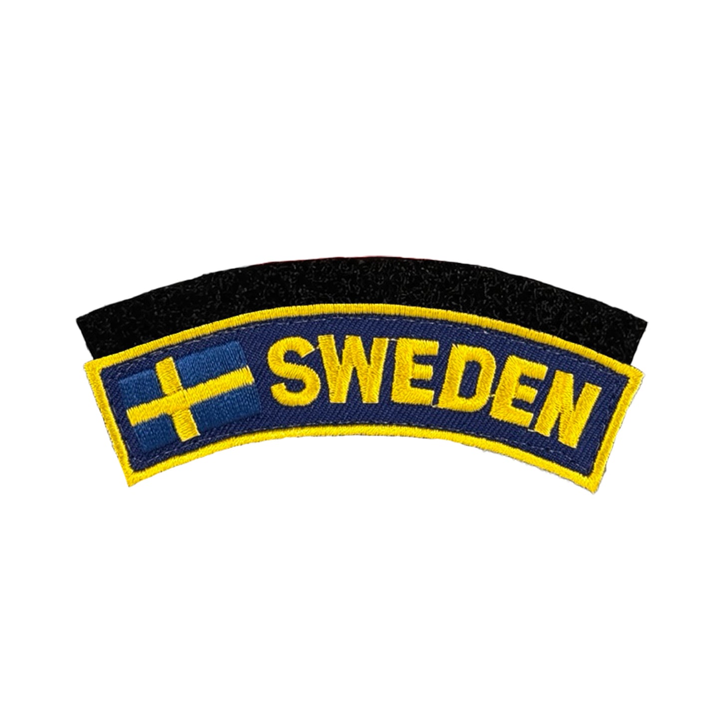 Broderat märke i blått med gul kant, med texten “SWEDEN” i gula bokstäver och en liten svensk flagga till vänster, samt svart kardborre baksida för enkel fastsättning.