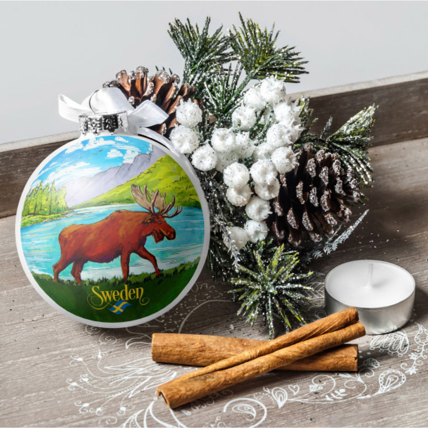 Stämningsfullt stileben med juldekorationen "Sweden stående älg", omgiven av kottar, gransris, kanelstänger och ett värmeljus.