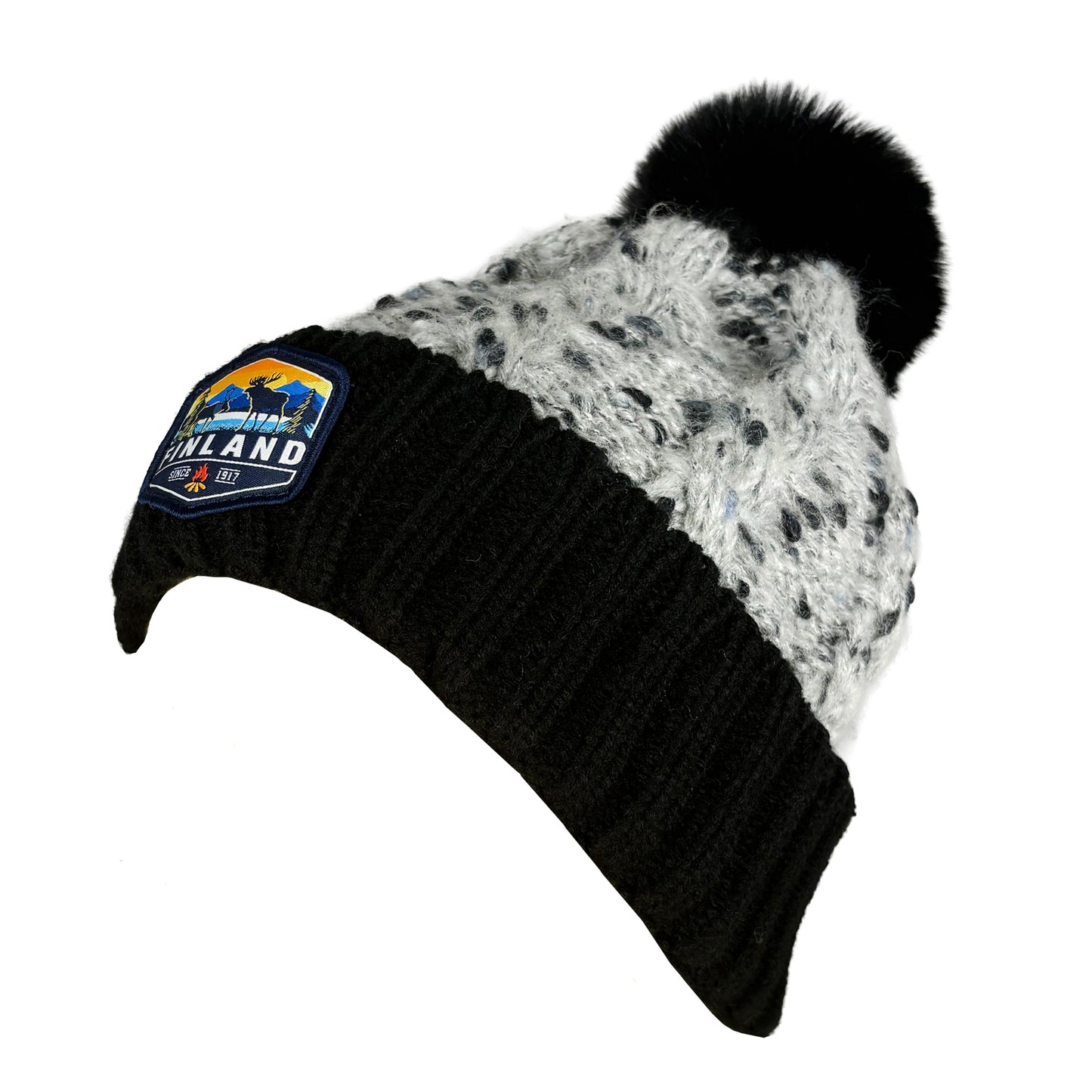 Stickad svart mössa med svart tofs och märke med texten Finland på mudden- sedd från sidan.