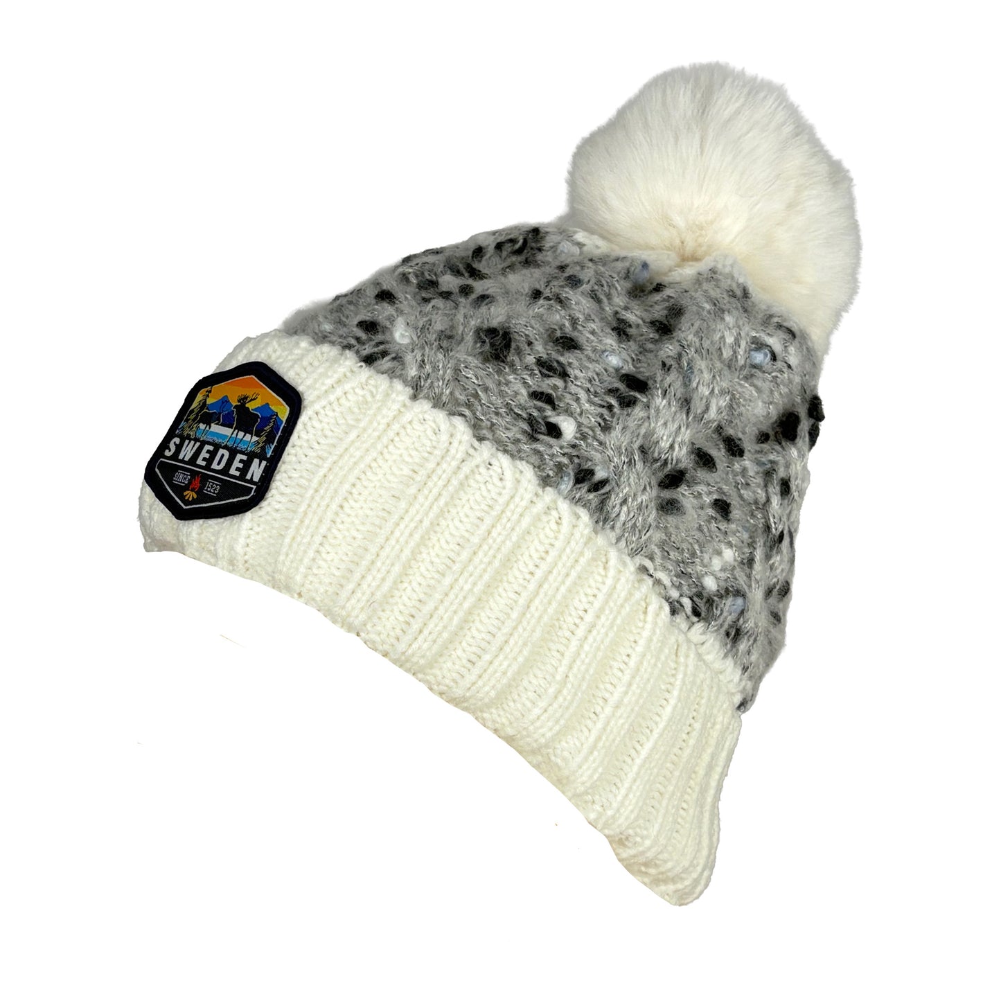 Stickad mössa i vitt och grått med fluffig vit tofs, sedd från sidan. Visar mössans passform och tofsens placering.