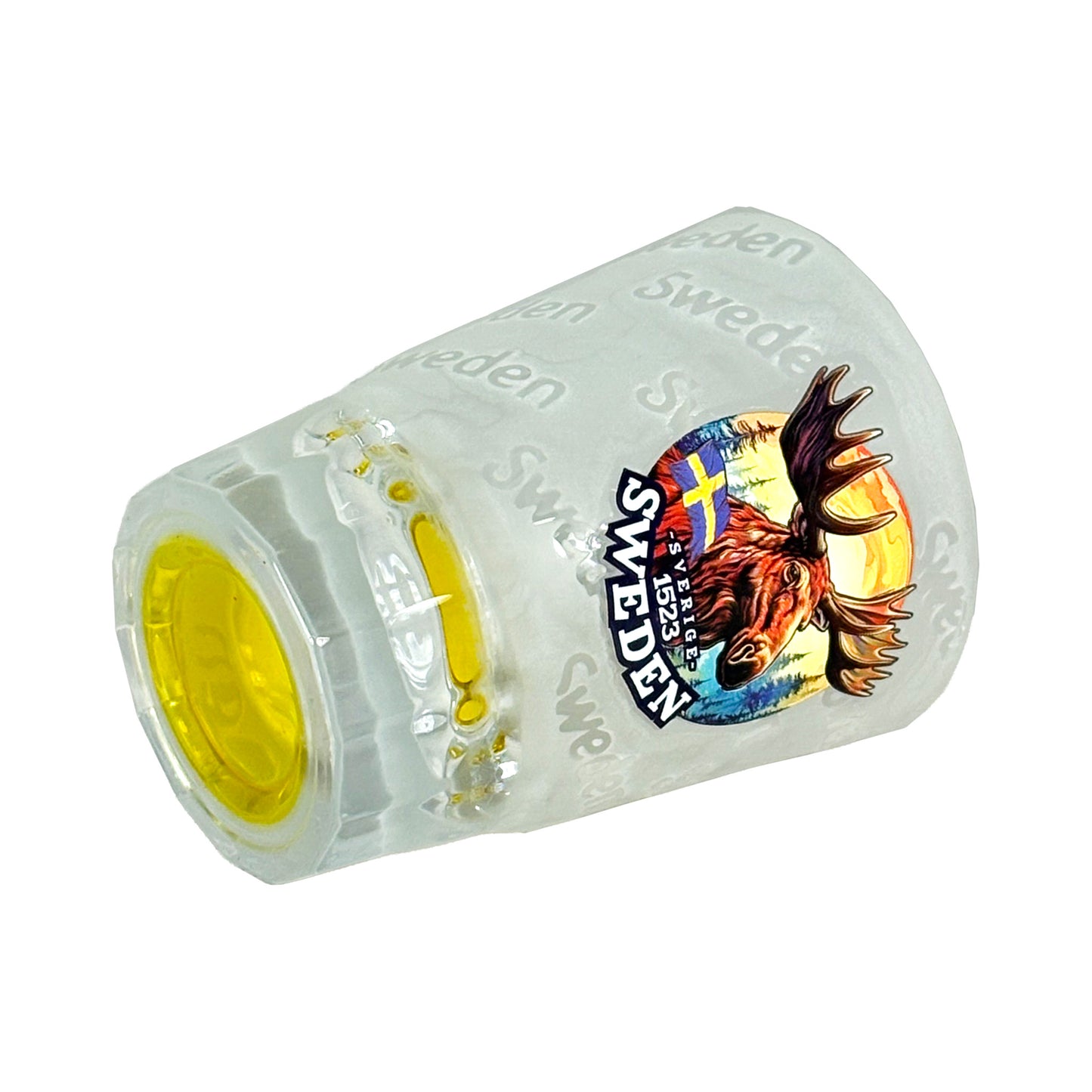 Shotglas liggande med gul botten synlig, frostat glas med motiv av älghuvud och texten "Sweden".