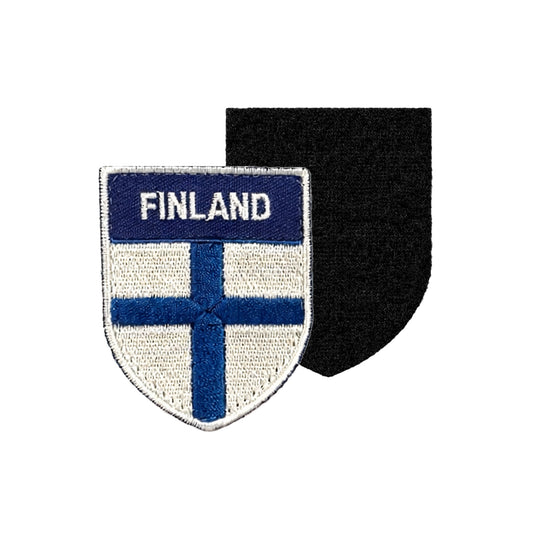 Broderat märke i sköldformat med vit bakgrund, blå finsk flagga och texten “FINLAND” i vitt på blå överdel, samt svart kardborrebaksida för enkel fastsättning