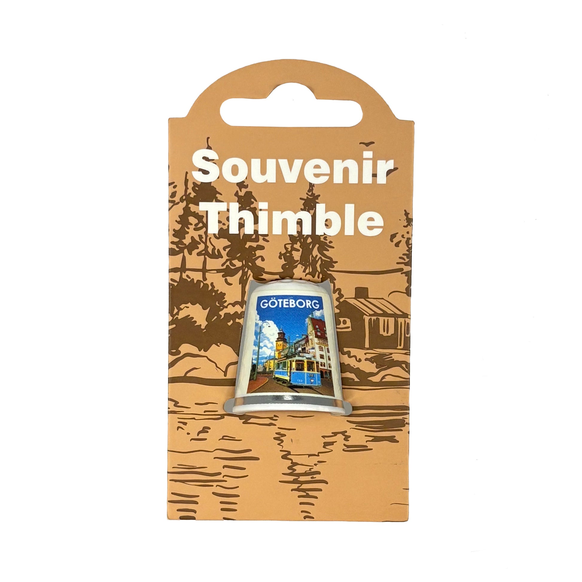 Vit fingerborg med motiv från staden Göteborg . Visas här i sin förpackning = en ljusbrun hängetikett med mörkbrunt skogsmotiv och texten Souvenir Thimble i vitt. 
