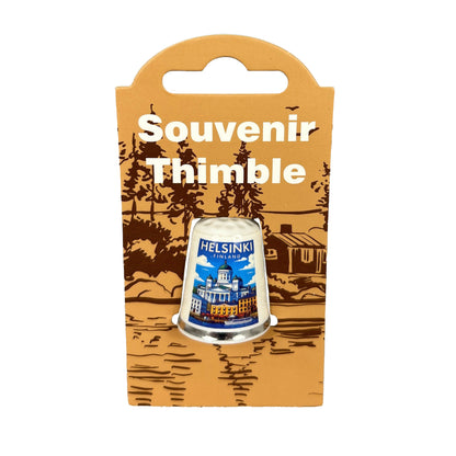 Vit fingerborg med silverkant och dekorativt motiv från Helsingfors. Visas här i sin förpackning md texten "Souvenir Thimble".
