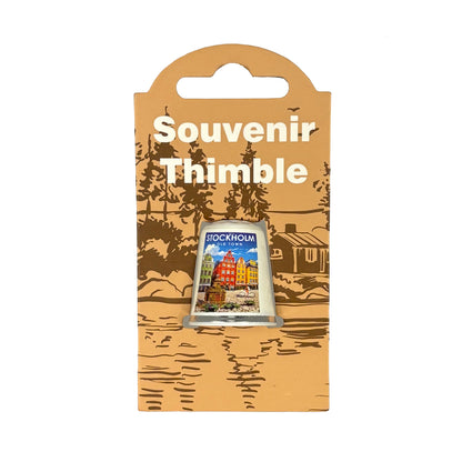 Fingerborg med motiv från Gamla Stan i Stockholm och texten "Stockholm Old Town". Perfekt som souvenir eller present. Visas här i sin förpackning = ljusbrun hängetikett med mörkbrunt skogsmotiv och texten "Souvenir Thimble" i vitt. 