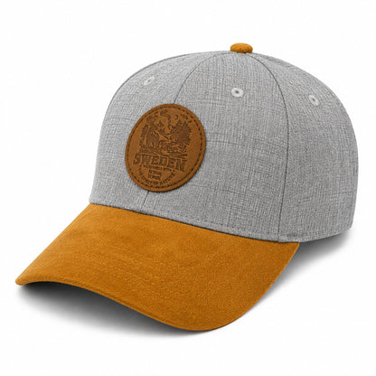Grå keps med brun skärm och runt lädermärke med naturmotiv och texten 'SWEDEN – wilderness with the Spirit of Nature'.