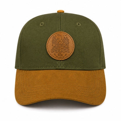 Grön keps med rund läderpatch med naturmotiv och texten “SWEDEN wilderness with the Spirit of Nature” sedd framifrån. Stilren keps med brun skärm.