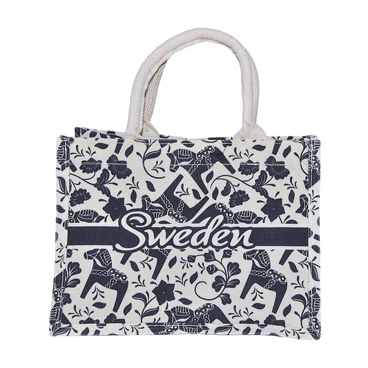 Vit handväska med motiv av blå dalahästar och texten Sweden. 