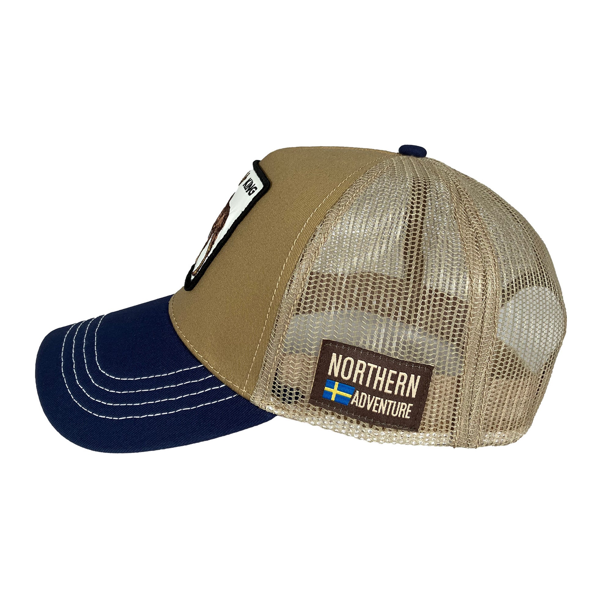 Ljusbrun och blå truckerkeps sedd från sidan. Här syns ett märke med texten “Northern Adventure” och  ensvensk flagga – en snygg keps med älgmotiv och justerbar nätbakdel.