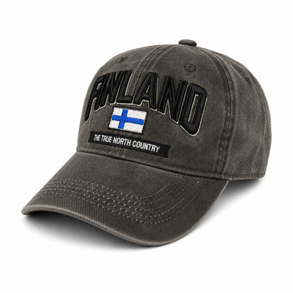 Grå vaxad keps sedd snett framifrån med broderad finsk flagga och texten Finland i 3D. Den vaxade ytan ger kepsen en distinkt look och känsla.