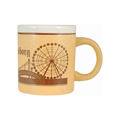 Ljusbrun keramikmugg med graverat motiv av pariserhjulet på Liseberg, samt skymtar av Ullevi, Älvsborgsbron och bokstäverna "borg" från texten Göteborg.