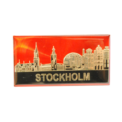 Epoxymagnet med Stockholms skyline i guld på röd bakgrund. Stilren och elegant souvenir med tydlig kontrast.