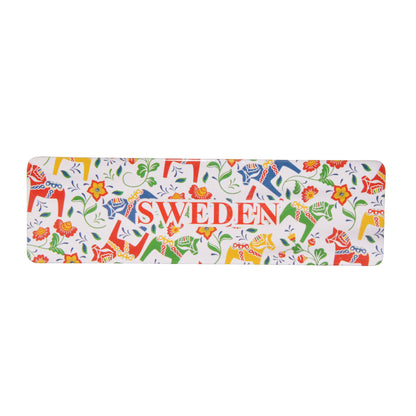 Rektangulär magnet med färgglada dalahästar omgivna av blommor och blad. 
