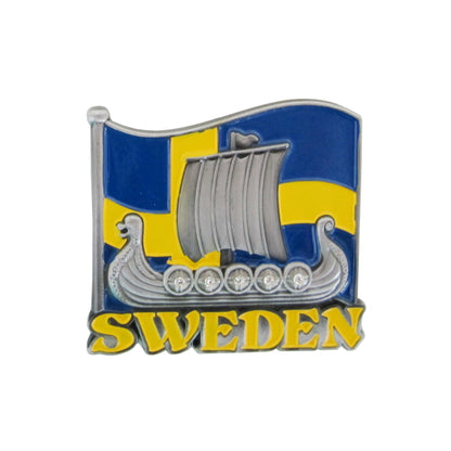 Bild på metallmagnet med vikingaskepp i 2D och svenska flaggan i bakgrunden. Vikingaskeppet är i tennfärg med dekorativa stenar på sköldarna.