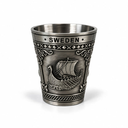 Metall-shotglas med 3 olika Sverigemotiv:  älg, karta och vikingaskepp. Här visas ena sidan av glaset som är dekorerat med ett vikingaskepp och texten Sweden. 