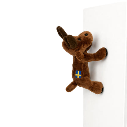 mörkbrun älg med broderad svensk flagga på ryggen och magneter i benen – en charmig och lekfull souvenir som fäster på kylskåp eller andra metalliska ytor. Sitter på en metallisk yta