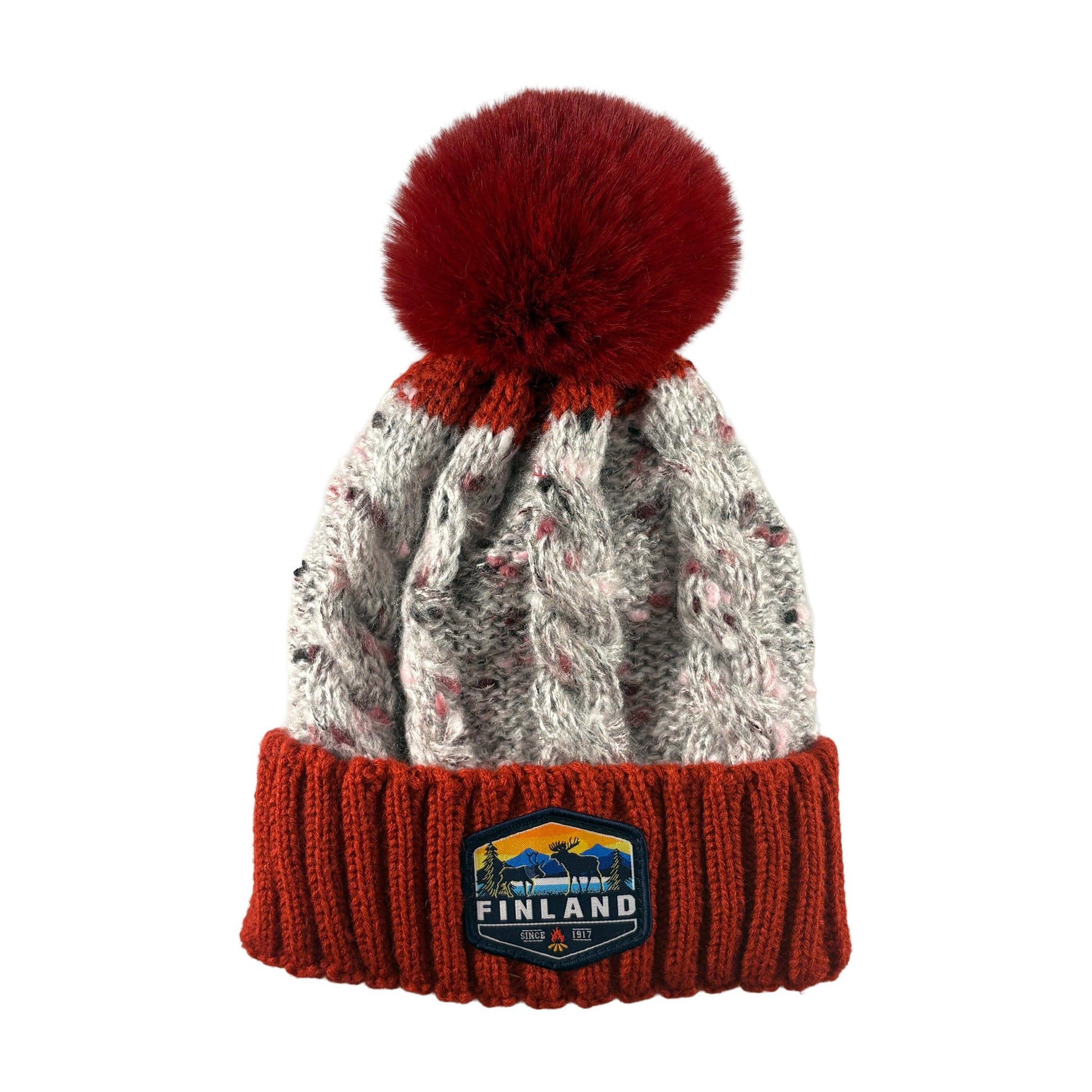 Stickad röd och grå mössa med röd tofs och ett märke med texten Finland på mudden - sedd framifrån. 