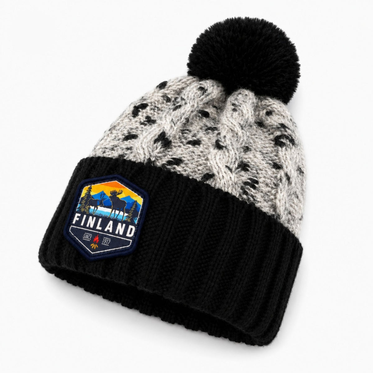 Stickad svart mössa med svart tofs och märke med texten Finland på mudden- sedd från sidan. 
