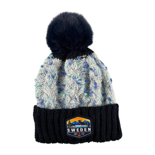 Stickad mössa i blått och grått med blå tofs, sedd framifrån. Märke med älgmotiv och texten "Sweden" synligt på mudden.