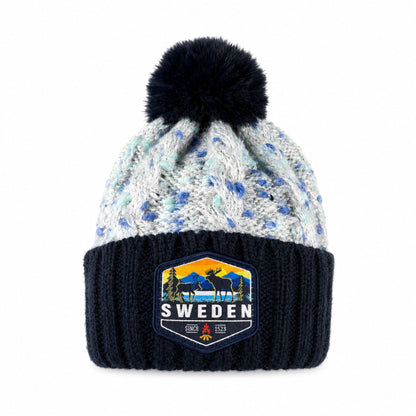 Stickad mössa i blått och grått med blå tofs, sedd framifrån. Märke med älgmotiv och texten "Sweden" synligt på mudden.