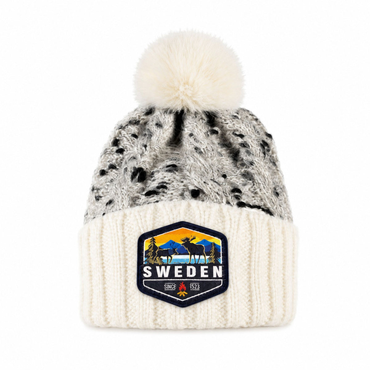 Stickad mössa i vitt och grått med fluffig vit tofs, sedd framifrån. Vävt märke med älgmotiv och texten "Sweden" synligt på mudden.