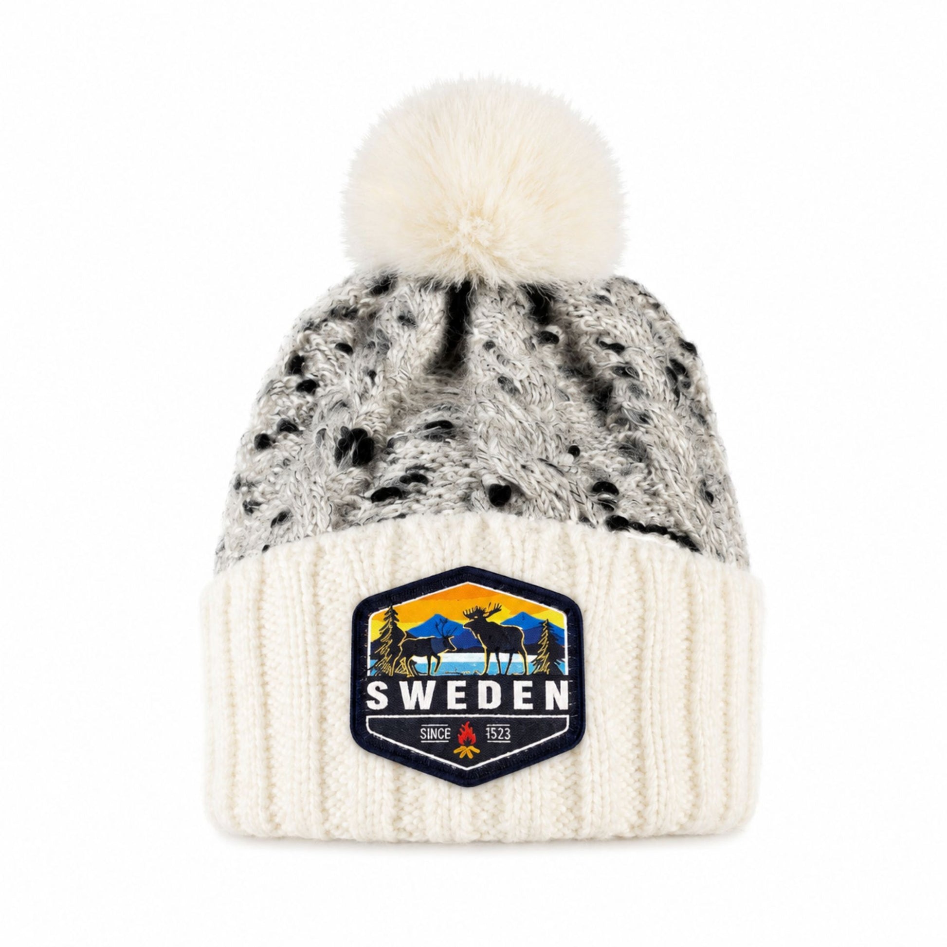 Stickad mössa i vitt och grått med fluffig vit tofs, sedd framifrån. Vävt märke med älgmotiv och texten "Sweden" synligt på mudden.