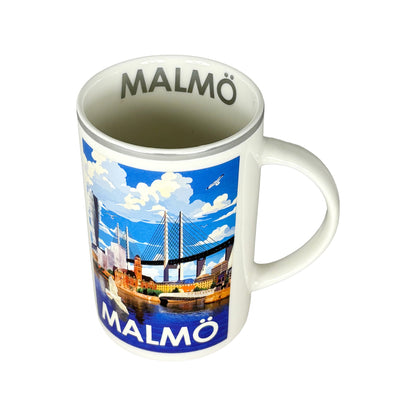 Souvenirmugg Malmö med silverkant sedd snett ovanifrån med silvrig text “Malmö” inuti muggen.