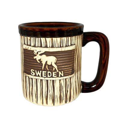 Mugg med älg och texten "SWEDEN". Den här muggen har ett träliknande utseende med handtag och kant upptill i mörkbrunt. 