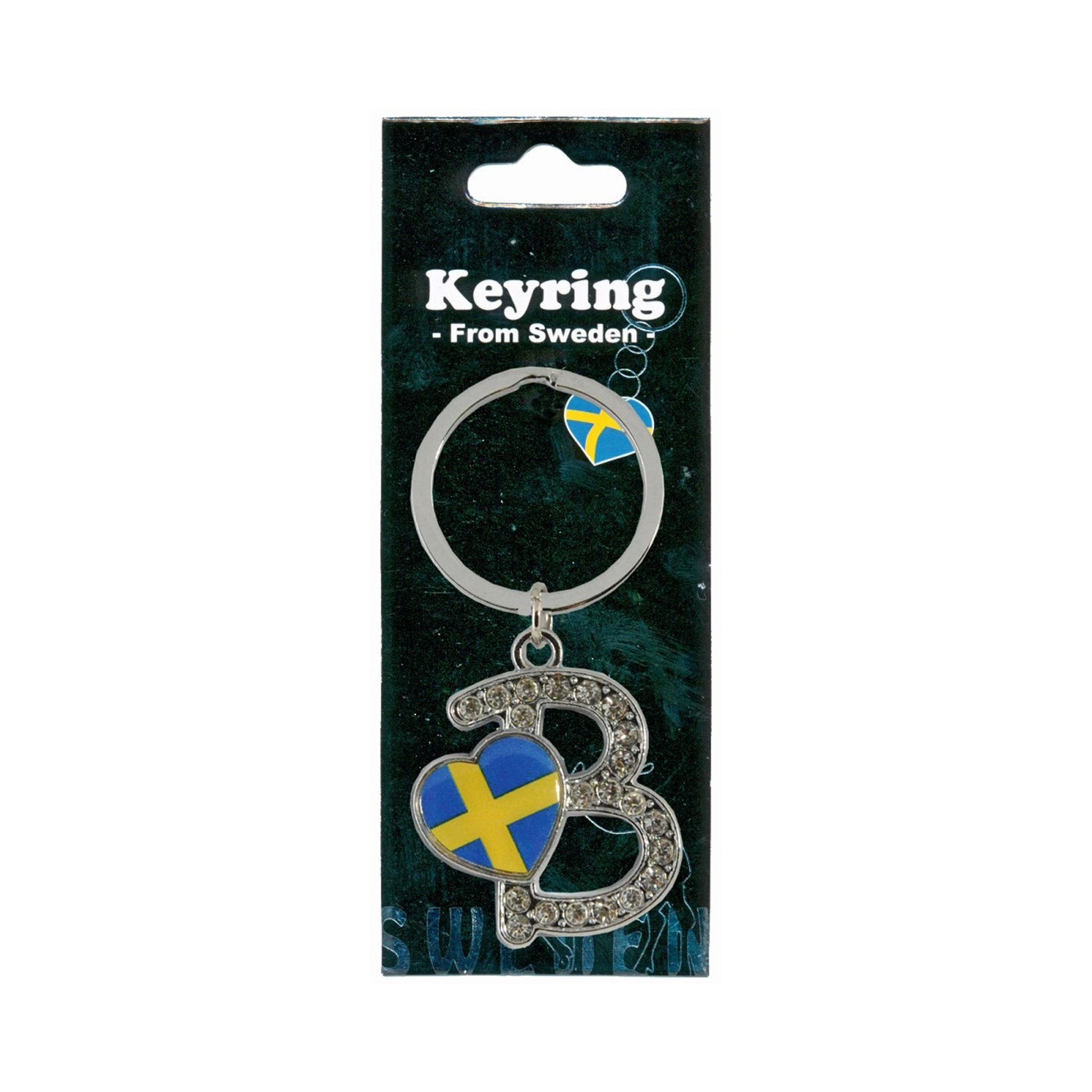 Metallnyckelring med bokstaven B. Bokstaven är dekorerad med glitterstenar. På bokstaven finns även ett hjärta med en svensk flagga. Visas här i sin förpackning. Svart förpackning med texten "Keyring from Sweden" i vitt. 