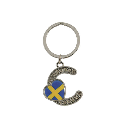 Metallnyckelring med bokstaven C. Bokstaven är dekorerad med glitterstenar. På bokstaven finns även ett hjärta med en svensk flagga.
