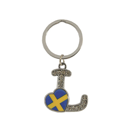Metallnyckelring med bokstaven L. Bokstaven är dekorerad med glitterstenar. På bokstaven finns även ett hjärta med en svensk flagga.