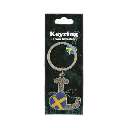 Metallnyckelring med bokstaven L. Bokstaven är dekorerad med glitterstenar. På bokstaven finns även ett hjärta med en svensk flagga. Visas här i sin förpackning. Svart förpackning med  texten "Keyring från Sweden" i vitt.
