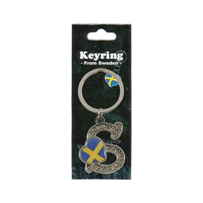 Metallnyckelring med bokstaven S. Bokstaven är dekorerad med glitterstenar. På bokstaven finns även ett hjärta med en svensk flagga. Visas här i sin förpackning. Svart förpackning med  texten "Keyring från Sweden" i vitt.