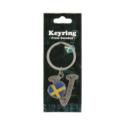 Metallnyckelring med bokstaven V. Bokstaven är dekorerad med glitterstenar. På bokstaven finns även ett hjärta med en svensk flagga. Visas här i sin förpackning. Svart förpackning med  texten "Keyring från Sweden" i vitt.