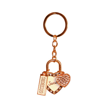 Souvenirnyckelring med två hjärtan – ett större med glittrig roseguldsram, vit mitt och texten Sweden, och ett mindre hjärta prytt med glitterstenar – samt en skylt med texten Göteborg.