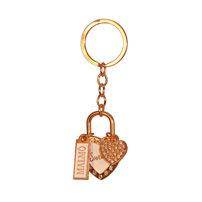 Souvenirnyckelring med två hjärtan – ett större med glittrig roseguldsram, vit mitt och texten Sweden, och ett mindre hjärta prytt med glitterstenar – samt en skylt med texten Malmö.