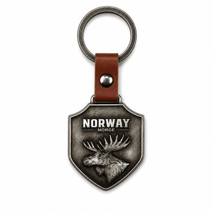 Nyckelring i metall som hänger i ett brunt läderband med metallring. Nyckelringen är sköld formad och pryds av texten "Norway - Norge" och ett älghuvud. 