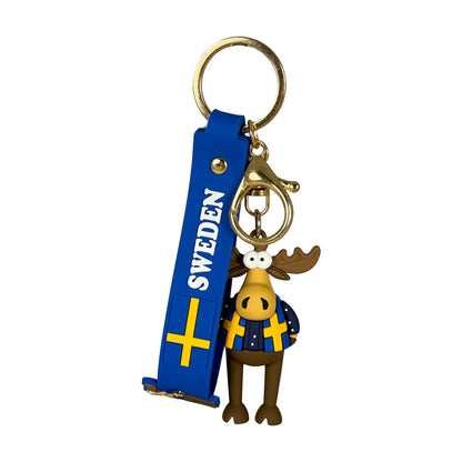 Nyckelring med tokrolig älgfigur klädd i jacka med svenska flaggor, fäst vid blå PVC rem med svensk flagga, texten "Sweden" och guldfärgad nyckelring. En lekfull och karaktärsfull accessoar med tydlig svensk prägel.