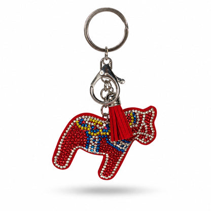 En röd, dalahäst formad nyckelring dekorerad med glittrande strass i rött, blått, gult och silver. Nyckelringen har en röd tofs samt en silverfärgad karbinhake och ring.