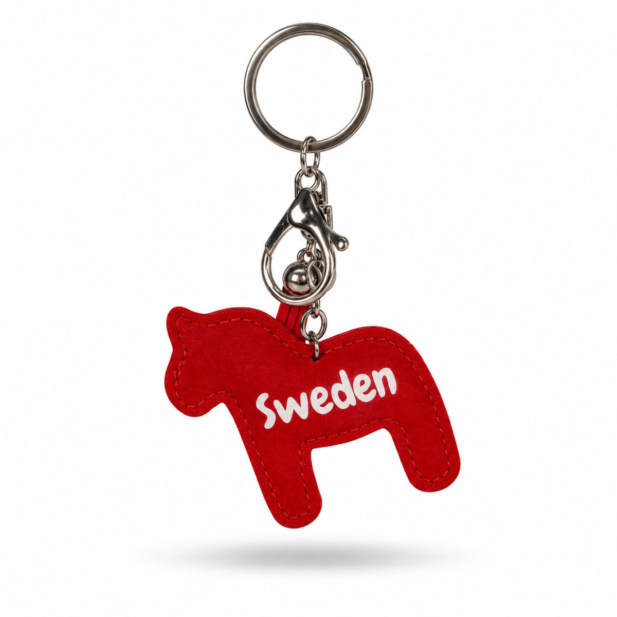 Baksidan av en röd, dalahäst formad nyckelring med texten "SWEDEN" på baksidan. Nyckelringen har en röd tofs samt en silverfärgad karbinhake och ring. 