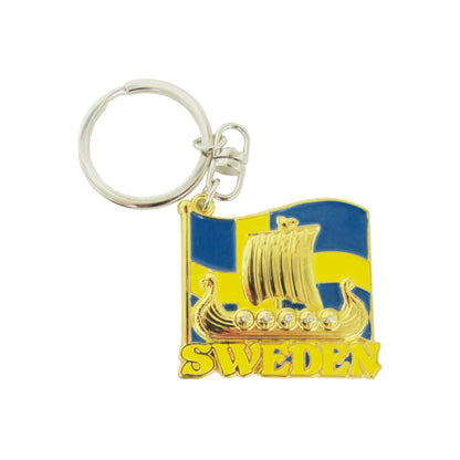 Metallnyckelring med guldfärgat vikingaskepp framför svensk flagga, dekorerad med små glitterstenar i sköldarna.