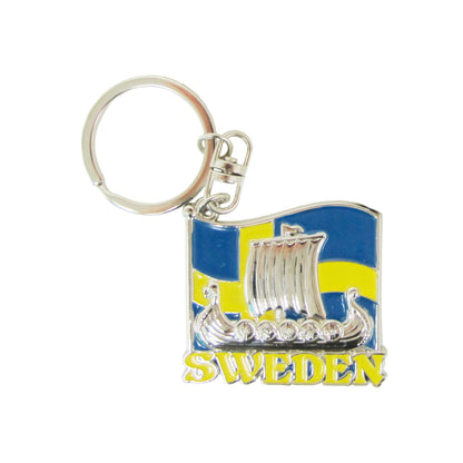 Metallnyckelring med silverfärgat vikingaskepp framför svensk flagga, dekorerad med små glitterstenar i sköldarna.