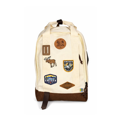 Beige ryggsäck med brun botten och snören. Läder och broderade märken med en älg och texten SWEDEN. Visas här rakt framifrån.