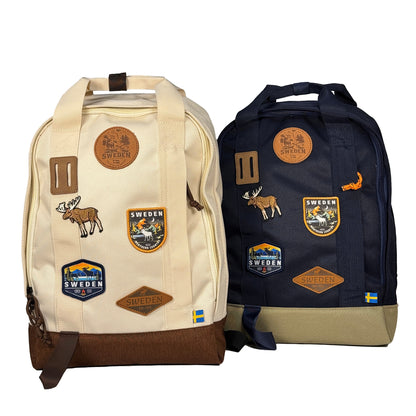 Blå och beige ryggsäck med läder och broderade märken med en älg och texten SWEDEN. 