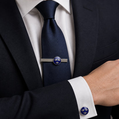 Silverfärgad slipsnål och manschettknapp med blå emalj och tre kronor-design, buren till kostym för en klassisk och stilren look.