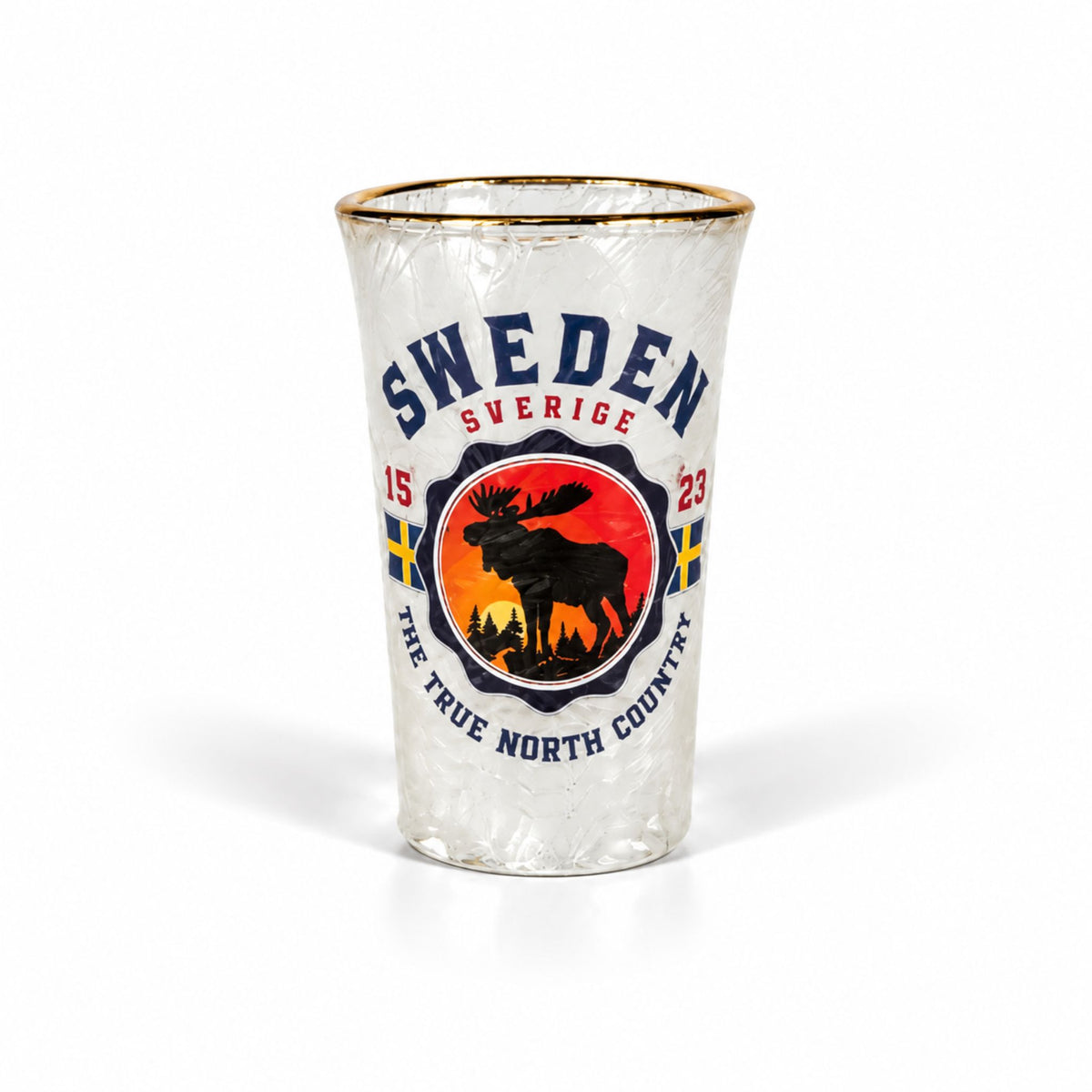 Stilfullt shotglas med frostad yta och guldkant, prytt med en älg på ett berg i solnedgången, två svenska flaggor, texten "SWEDEN – The True North Country" och årtalet 1523.
