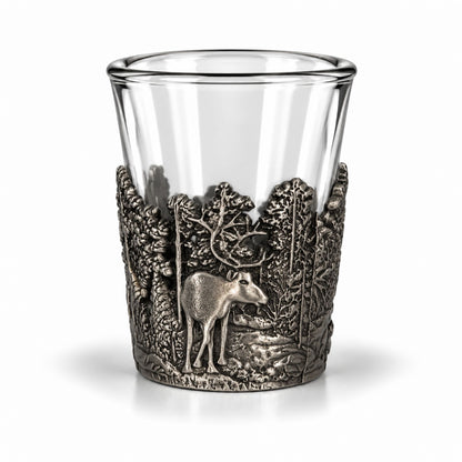 Shotsglas i glas med ett omslag i tennfärgad metall fotat ur ytterliga en annan vinkel, här visas glasets skogsmotiv med en ren sedd framifrån.