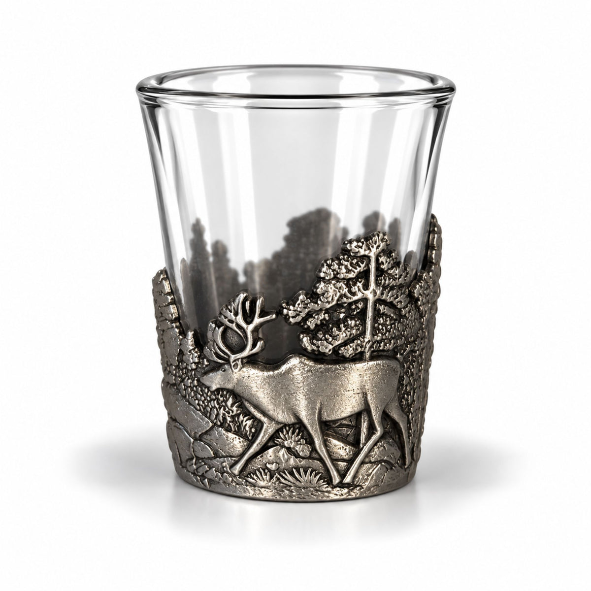 Shotsglas i glas med ett omslag i tennfärgad metall fotat ur en annan vinkel, här visas glasets skogsmotiv med en ren sedd från sidan. 