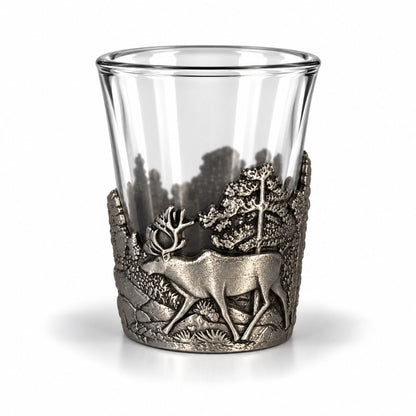 Shotsglas i glas med ett omslag i tennfärgad metall fotat ur en annan vinkel, här visas glasets skogsmotiv med en ren sedd från sidan. 