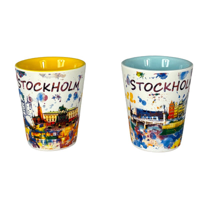 Två shotglas med Stockholmmotiv – ett med ljusblå insida och ett med gul insida, placerade sida vid sida.
